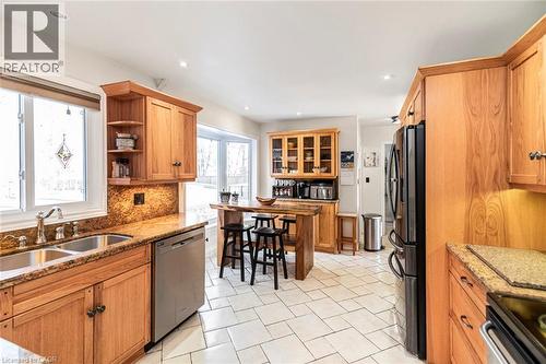 Kitchen with light stone countertops, brown cabinetry, appliances with stainless steel finishes, tasteful backsplash, and open shelves - 7087 Rainham Road, Dunnville, ON - Indoor Photo Showing Kitchen With Double Sink