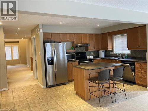 Kitchen featuring appliances with stainless steel finishes, a breakfast bar, brown cabinetry, a center island, and tasteful backsplash - 421 White Birch Avenue, Waterloo, ON - Indoor Photo Showing Kitchen With Double Sink