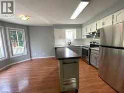 Kitchen with appliances with stainless steel finishes, dark countertops, light wood-style floors, white cabinetry, and under cabinet range hood - 