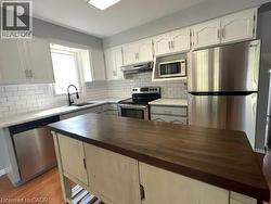 Kitchen featuring stainless steel appliances, backsplash, white cabinets, and butcher block countertops - 