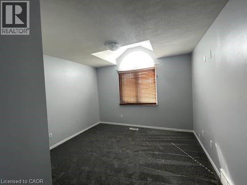 Empty room featuring a textured ceiling, dark carpet, and a baseboard radiator - 214 Benesfort Crescent, Kitchener, ON - Indoor Photo Showing Other Room