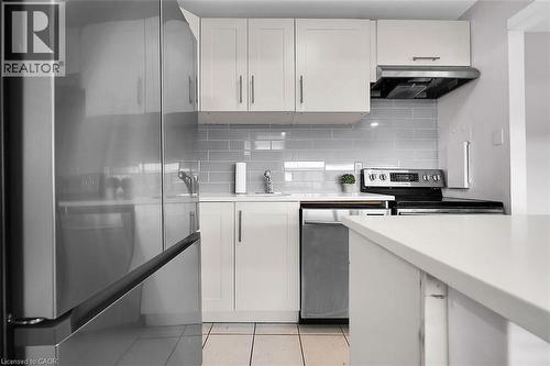 Kitchen featuring white cabinets, range hood, decorative backsplash, and appliances with stainless steel finishes - 15 Albright Road Unit# 811, Hamilton, ON 
