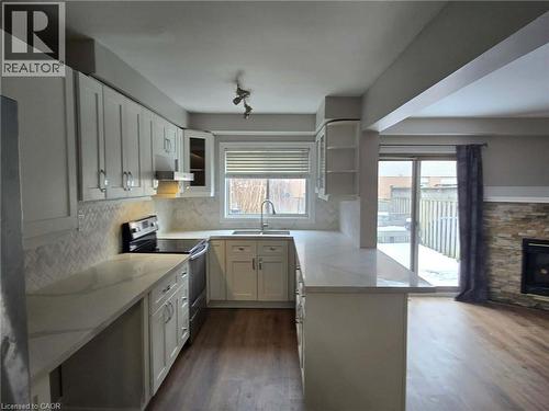 Kitchen with stainless steel range with electric stovetop, a peninsula, white cabinets, and dark wood-style flooring - 185 Sulmona Drive, Hamilton, ON - Indoor Photo Showing Kitchen With Fireplace