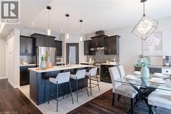 Kitchen featuring a kitchen breakfast bar, stainless steel appliances, an island with sink, decorative light fixtures, and light wood finished floors - 
