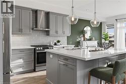 Kitchen featuring gray cabinetry, stainless steel appliances, wall chimney exhaust hood, light wood-style flooring, and hanging light fixtures - 