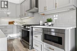 Kitchen featuring appliances with stainless steel finishes, wall chimney range hood, backsplash, light wood-type flooring, and light stone countertops - 