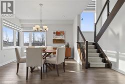 Dining space with healthy amount of natural light, stairway, dark wood finished floors, and a chandelier - 