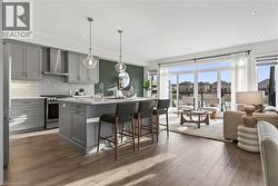 Kitchen featuring gray cabinets, a breakfast bar, appliances with stainless steel finishes, wall chimney exhaust hood, and recessed lighting - 