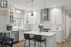 Kitchen with pendant lighting, wine cooler, wall chimney range hood, appliances with stainless steel finishes, and white cabinetry - 