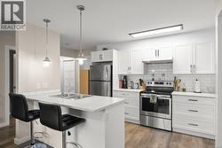 Suite Kitchen with appliances with stainless steel finishes, a kitchen breakfast bar, light countertops, a peninsula, and white cabinetry - 