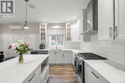 Kitchen featuring appliances with stainless steel finishes, white cabinets, decorative light fixtures, wall chimney range hood, and light stone counters - 