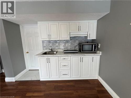 Kitchen with white cabinetry, backsplash, stainless steel microwave, under cabinet range hood, and dark wood-style flooring - 211 Snowdrop Crescent Unit# Lower, Kitchener, ON - Indoor Photo Showing Kitchen