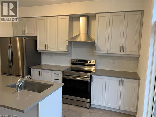 Kitchen featuring stainless steel appliances, wall chimney range hood, decorative backsplash, light wood-style floors, and dark stone countertops - 49 Eberhardt Drive, Wasaga Beach, ON - Indoor Photo Showing Kitchen