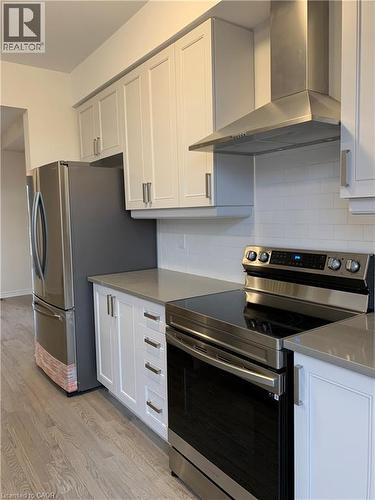 Kitchen featuring appliances with stainless steel finishes, wall chimney exhaust hood, light wood-type flooring, backsplash, and light stone countertops - 49 Eberhardt Drive, Wasaga Beach, ON - Indoor Photo Showing Kitchen
