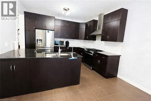 Kitchen featuring stainless steel appliances, wall chimney range hood, dark brown cabinets, and dark stone countertops - 127 Elmbank Trail Unit# Upper, Kitchener, ON - Indoor Photo Showing Kitchen With Double Sink