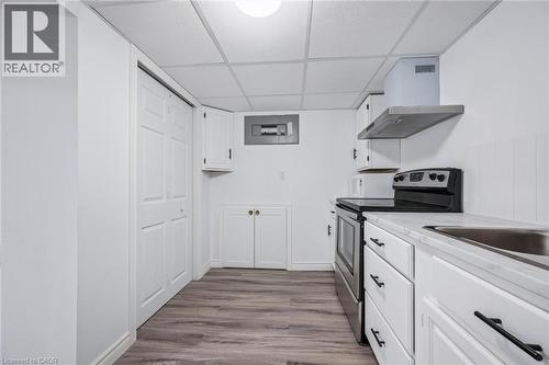 Kitchen with stainless steel range with electric stovetop, white cabinetry, light countertops, a drop ceiling, and wall chimney exhaust hood - 21 Forest Glen Court, Kitchener, ON - Indoor Photo Showing Kitchen