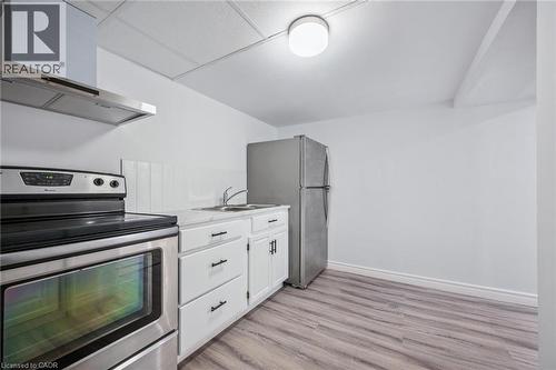 Kitchen featuring appliances with stainless steel finishes, wall chimney exhaust hood, light countertops, white cabinetry, and light wood finished floors - 21 Forest Glen Court, Kitchener, ON - Indoor Photo Showing Kitchen With Double Sink