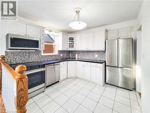 Kitchen with appliances with stainless steel finishes, a textured ceiling, glass insert cabinets, pendant lighting, and white cabinetry - 773 Queensdale Avenue E, Hamilton, ON - Indoor Photo Showing Kitchen