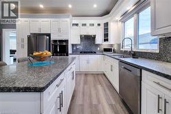 Kitchen featuring appliances with stainless steel finishes, dark stone countertops, glass insert cabinets, recessed lighting, and white cabinetry - 
