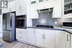 Kitchen featuring glass insert cabinets, appliances with stainless steel finishes, white cabinetry, and light wood finished floors - 