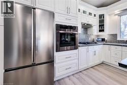 Kitchen with stainless steel appliances, glass insert cabinets, white cabinets, under cabinet range hood, and crown molding - 