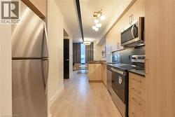 Kitchen featuring dark countertops, stainless steel appliances, a peninsula, light brown cabinetry, and modern cabinets - 