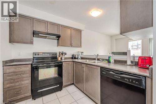 Kitchen with black appliances, under cabinet range hood, light tile patterned floors, and dark countertops - 23 Kingsbury Square Unit# 23, Guelph, ON - Indoor Photo Showing Kitchen With Double Sink