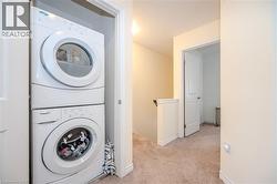 Laundry area featuring stacked washer / drying machine, light carpet, and radiator heating unit - 