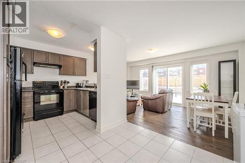 Kitchen featuring light tile patterned flooring, black appliances, open floor plan, dark brown cabinetry, and under cabinet range hood - 23 Kingsbury Square Unit# 23, Guelph, ON - Indoor