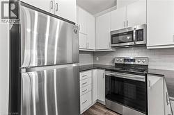 Kitchen featuring appliances with stainless steel finishes, dark countertops, white cabinets, and backsplash - 
