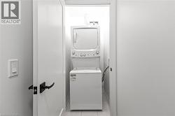 Laundry room with stacked washer / dryer and light tile patterned floors - 