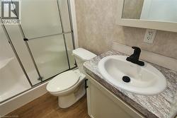 Full bath featuring a shower stall, vanity, dark wood-type flooring, and a textured wall - 