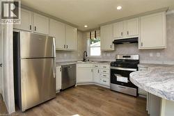 Kitchen featuring appliances with stainless steel finishes, light countertops, dark wood-style floors, under cabinet range hood, and recessed lighting - 