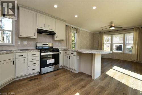 Kitchen with a peninsula, stainless steel range with gas stovetop, dark wood finished floors, under cabinet range hood, and ceiling fan - 1085 Concession 10 Road W Unit# 23, Flamborough, ON - Indoor Photo Showing Kitchen