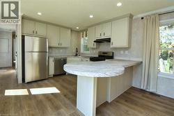 Kitchen featuring a peninsula, light countertops, appliances with stainless steel finishes, dark wood-style flooring, and under cabinet range hood - 