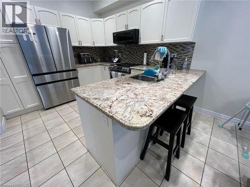 Kitchen with stainless steel appliances, a peninsula, a kitchen bar, white cabinets, and light stone counters - 24 Hazelton Avenue, Hamilton, ON - Indoor Photo Showing Kitchen With Upgraded Kitchen