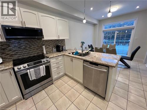 Kitchen with stainless steel appliances, a peninsula, white cabinetry, light stone counters, and decorative light fixtures - 24 Hazelton Avenue, Hamilton, ON - Indoor Photo Showing Kitchen With Stainless Steel Kitchen With Double Sink With Upgraded Kitchen