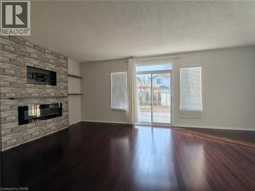Unfurnished living room with a textured ceiling, a fireplace, and dark wood-style floors - 563 Dansbury Drive, Waterloo, ON 
