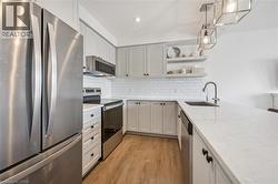 Kitchen with appliances with stainless steel finishes, pendant lighting, open shelves, light stone countertops, and light wood-style flooring - 