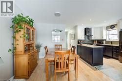 Kitchen with wall chimney exhaust hood, decorative backsplash, light wood-type flooring, white cabinetry, and decorative light fixtures - 