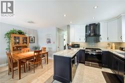 Kitchen featuring appliances with stainless steel finishes, white cabinets, decorative backsplash, wall chimney exhaust hood, and a peninsula - 