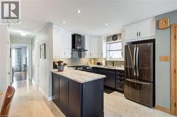 Kitchen featuring white cabinetry, stainless steel appliances, wall chimney exhaust hood, light stone countertops, and recessed lighting - 