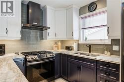 Kitchen with white cabinetry, stainless steel gas range oven, wall chimney range hood, and light stone countertops - 