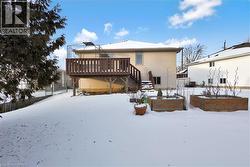 Snow covered rear of property with a vegetable garden, a wooden deck, and stairs - 