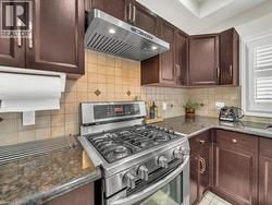 Kitchen with stainless steel gas range oven, dark brown cabinetry, range hood, and dark stone countertops - 