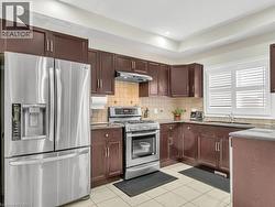 Kitchen featuring appliances with stainless steel finishes, dark brown cabinetry, tasteful backsplash, under cabinet range hood, and light tile patterned flooring - 