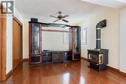 Unfurnished living room featuring a wood stove, hardwood / wood-style floors, and ceiling fan - 