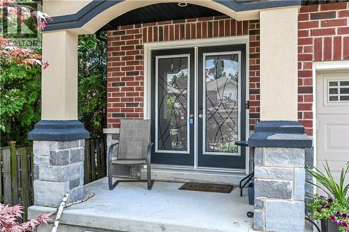 Brick facade entryway with a concrete porch, featuring double entry doors with decorative glass inserts, stucco-finished columns, and stone pillar bases - 71 Jessica Street, Hamilton, ON - Outdoor With Deck Patio Veranda