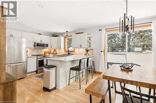 Kitchen with hanging light fixtures, appliances with stainless steel finishes, a peninsula, light wood-style floors, and white cabinetry - 230 Saugeen Street, Grey Highlands, ON - Indoor
