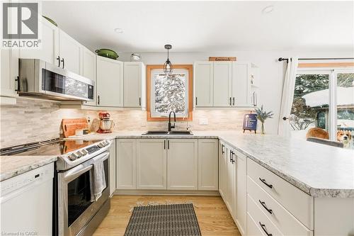 Kitchen with stainless steel appliances, pendant lighting, a peninsula, light countertops, and light wood-style flooring - 230 Saugeen Street, Grey Highlands, ON - Indoor Photo Showing Kitchen